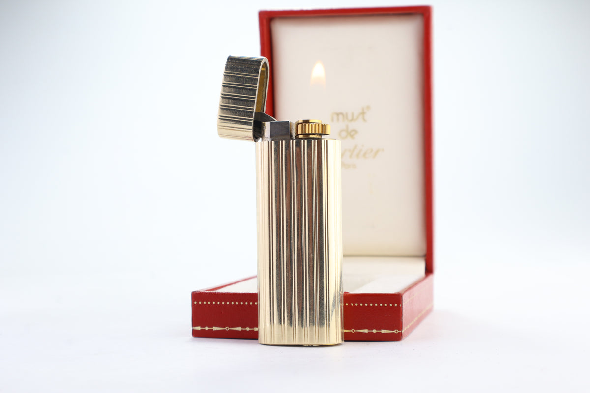 Cartier Le Must gold lighter open and lit, showing the flame and the godron ribbed jacket