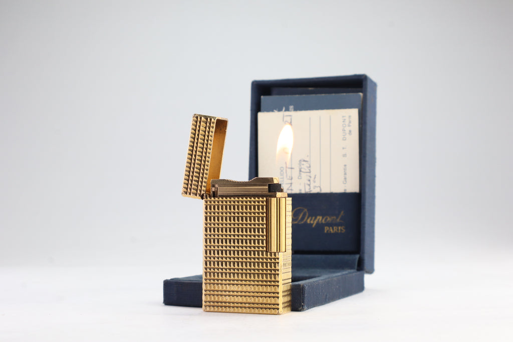 S.T. Dupont Ligne 1 BR gold lighter open and lit, beside its navy box