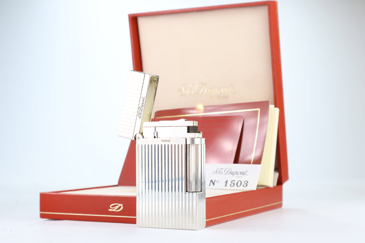 S.T. Dupont Ligne 2 Montparnasse silver lighter open and lit, beside its red box and papers